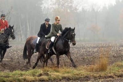 Reiter in Jagdkleidung galoppieren über ein nebliges Feld